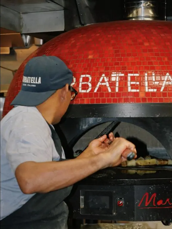 Pizzaiolo working the red-tiled wood-fire oven