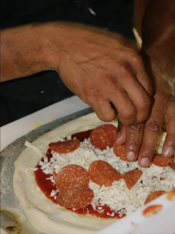 Hands topping a pizza before it goes in the oven